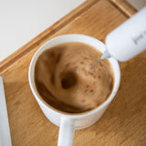 white froth'y hand frother being used to make a latte in a white mug on a wooden cutting board