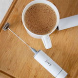 white froth'y hand frother next to a latte in a white mug on a wooden cutting board