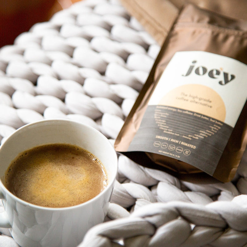 a cup of joe'y coffee alternative as a latte next to a bag of joe'y on a gray weighted blanket
