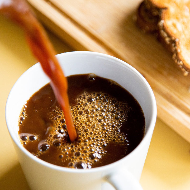 coffee alternative being poured into a white mug next to a piece of toast